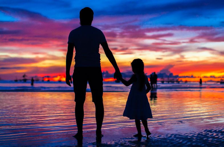 Silhouette of a little girl holding her father's hand and following him on a sunset beach